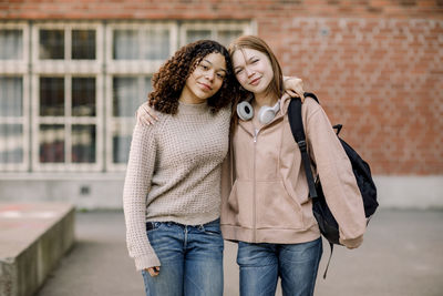 Portrait of smiling female students standing with arms around in high school campus