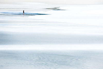 Distant view of man standing at frozen beach