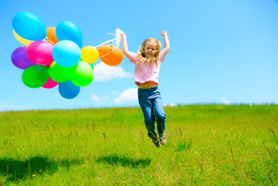 Full length of happy girl with balloons in field