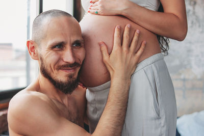 Close-up of smiling man listening to pregnant woman abdomen