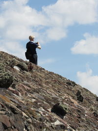 Low angle view of man standing on cliff against sky