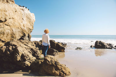 Rear view of woman standing by rock at beach