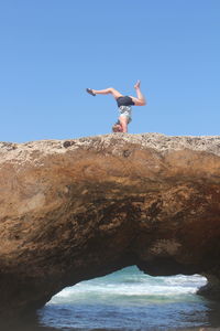 Woman doing handstand at rock formation against clear sky