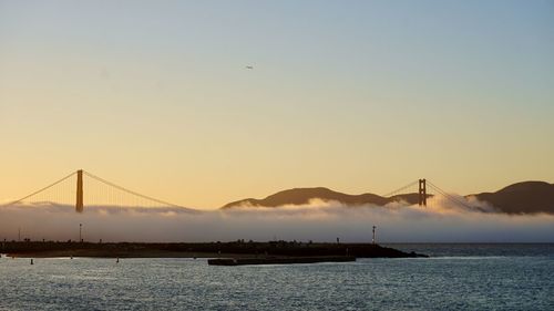 Silhouette bridge over sea against sky during sunset