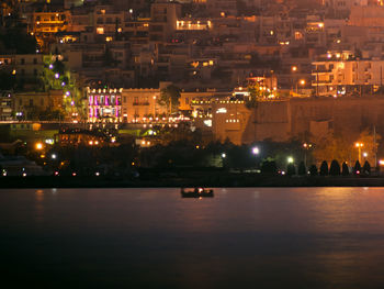 Illuminated cityscape by river against sky at night