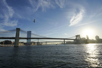 Suspension bridge over river against cloudy sky