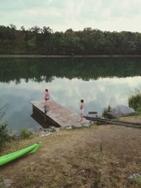 People sitting by lake against trees