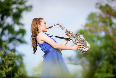 Side view of young bride playing saxophone in park