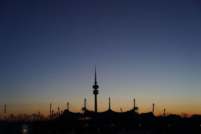 Silhouette of communications tower in city against clear sky