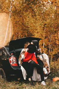 A romantic couple in love in warm sweaters is walking traveling by car in the autumn forest in fall