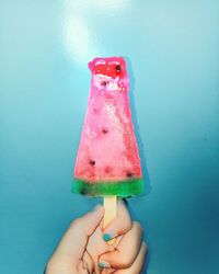 Close-up of hand holding ice cream against blue background