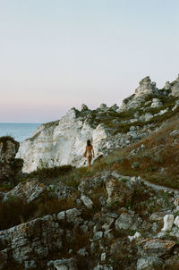 Naked woman walking on rock formation against clear sky