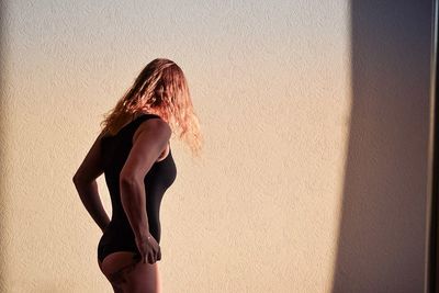 Side view of woman wearing swimsuit against wall
