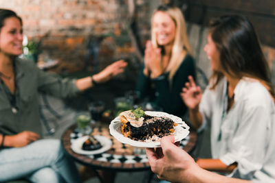 Cropped hand serving dessert to female friends sitting at outdoor restaurant during night