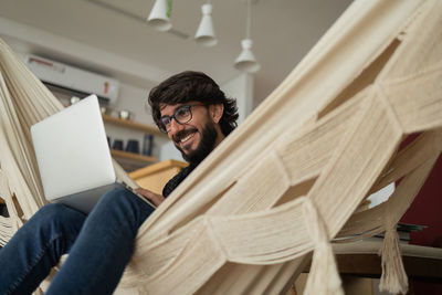 Young man  black glasses working with laptop on a white hammock notebook for working. home office