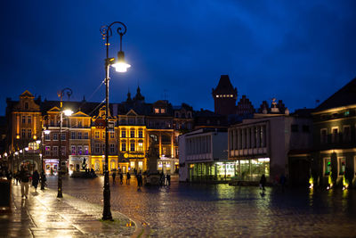 Illuminated street by buildings in city at night