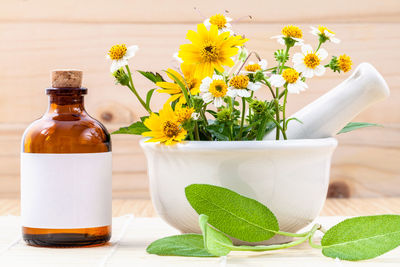 Close-up of flowers in mortar and pestle by bottle on table