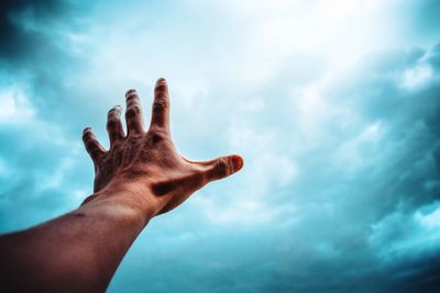 Low angle view of human hand against storm clouds