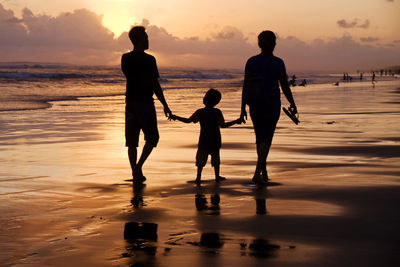 Silhouette people on beach against sky during sunset