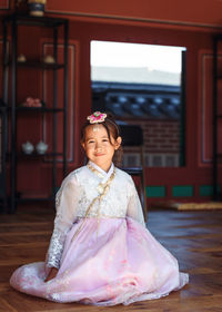 Full length of smiling girl in traditional clothes sitting indoors