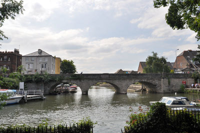 Arch bridge over river by buildings against sky