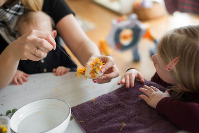 Midsection of woman with children making easter egg with petals