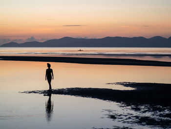 Silhouette woman standing at beach against sky during sunset
