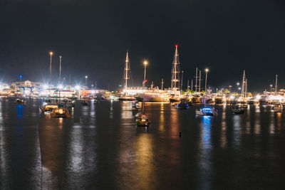 Sailboats in sea against illuminated buildings at night