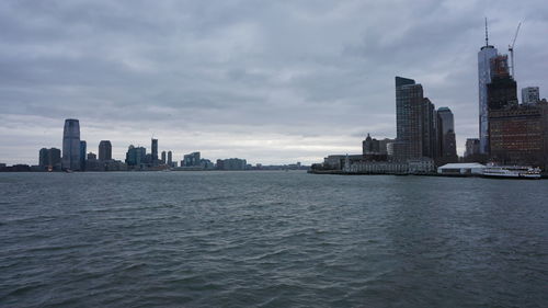 Modern buildings in front of river against cloudy sky at dusk in city