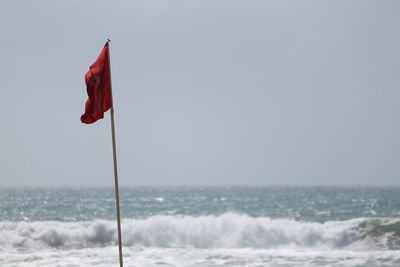 Red flag by sea against clear sky