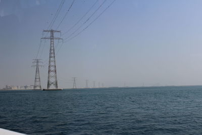 Electricity pylon by sea against clear sky