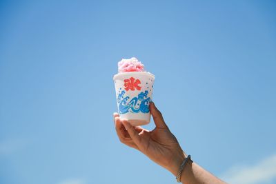 Person holding ice cream against blue sky