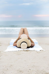 Pregnant woman wearing bikini and sunhat laying on beach