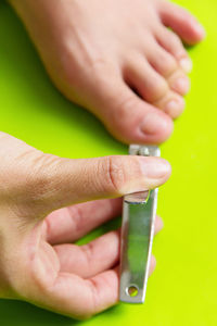 Close-up of person cutting fingernails over green background