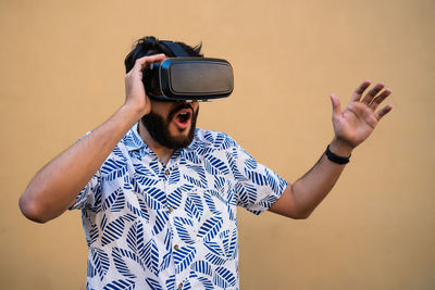 Young man wearing virtual reality simulator standing against wall outdoors