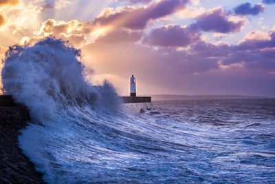 Waves splashing against cloudy sky during sunset