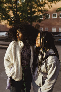 Teenage female friends looking away while standing on footpath