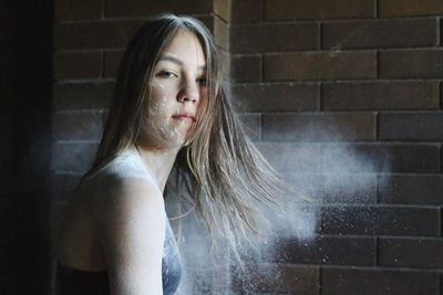 Portrait of teenage girl amidst powder in mid-air against brick wall