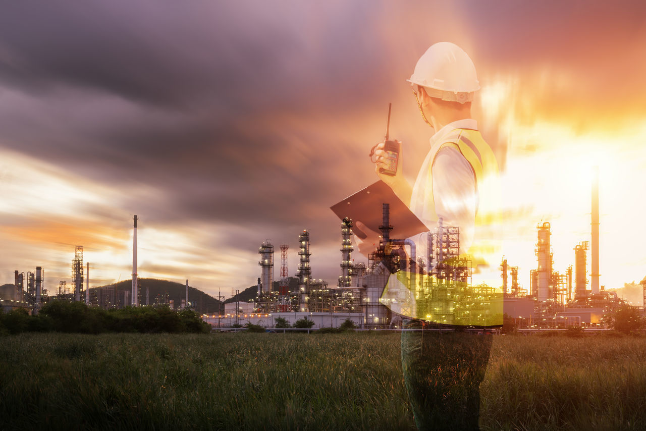 ILLUMINATED INDUSTRY ON FIELD AGAINST SKY DURING SUNSET