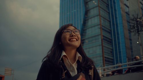 Portrait of smiling young woman looking away against building