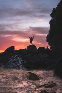 Silhouette man on cliff by sea against sky during sunset