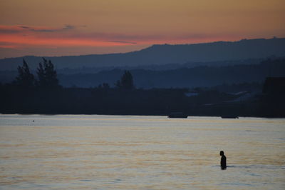 Silhouette man in sea against sky during sunset