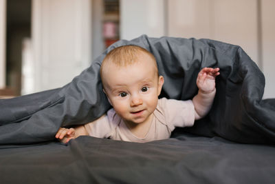 Cute baby is lying on his tummy, leaning on his wrists under the blanket