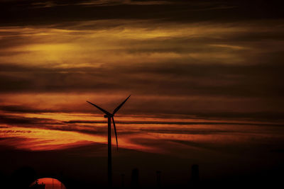 Silhouette of wind turbine against cloudy sky during sunset