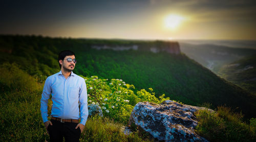 Man standing on landscape against sky during sunset