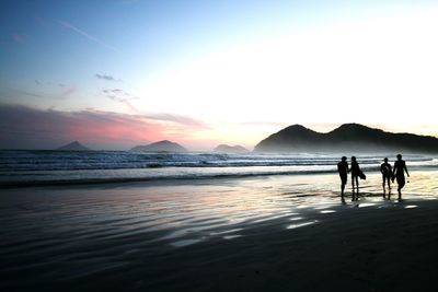 Silhouette people walking on beach against sky during sunset