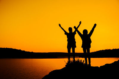 Silhouette people by sea against sky during sunset