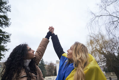 Female friends holding hands against sky