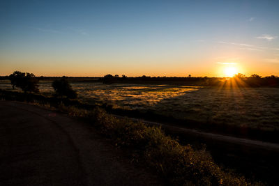 Scenic view of road by field against sky during sunset