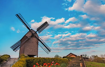 Windmill on landscape against blue sky and clouds